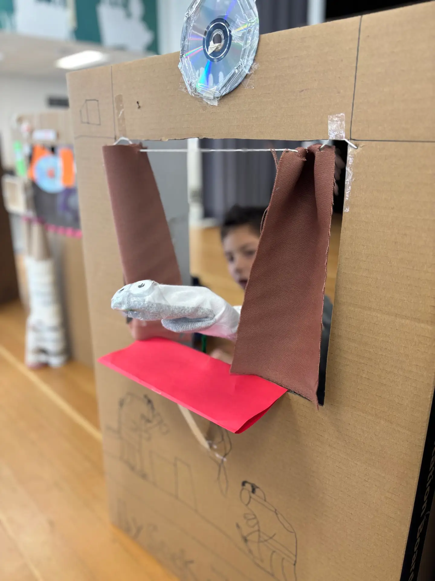 IMG_7751 A student proudly displays their sock puppet through a handmade theater.
