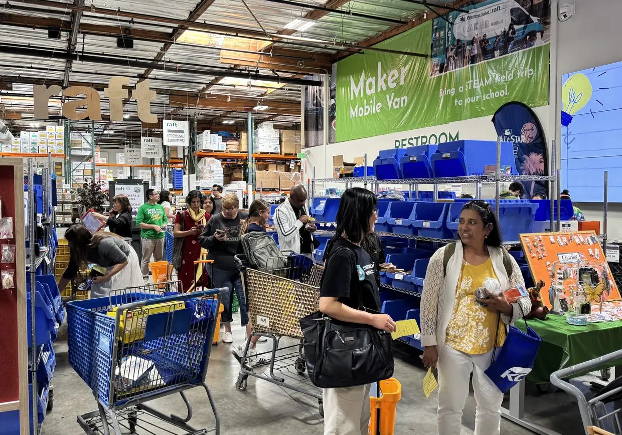 Shoppers browsing bins of upcycled classroom supplies in the RAFT warehouse store beneath the Maker Mobile Van banner