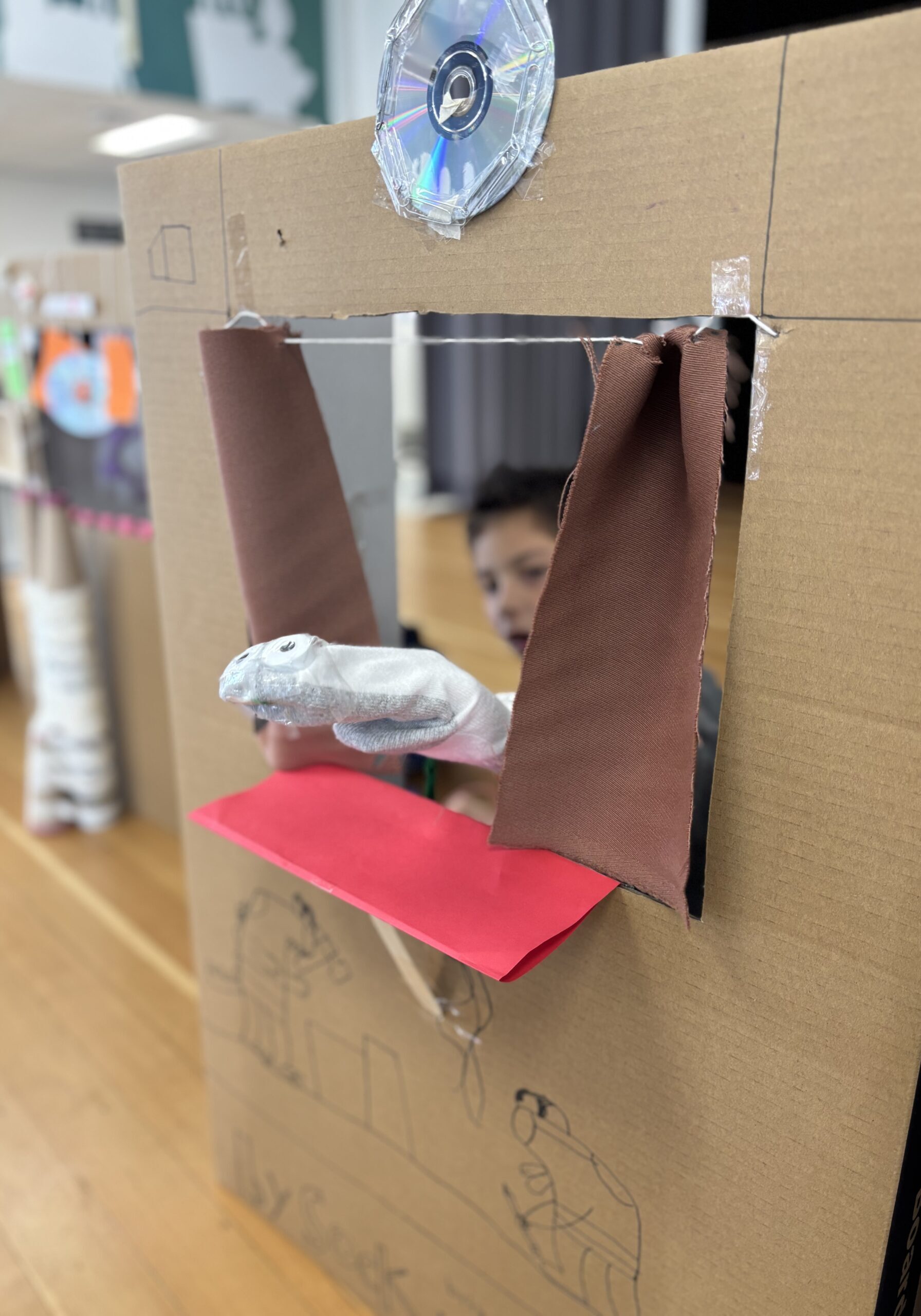 A student proudly displays their sock puppet through a handmade theater.